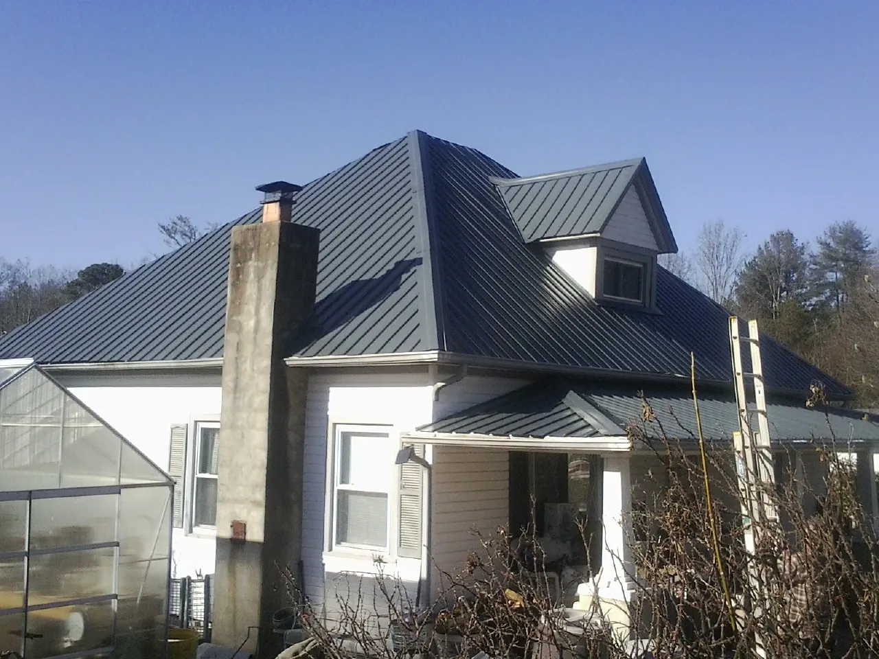Dark blue standing seam metal roof on a white farmhouse with dormer — Slate & Tile Roof Repair by Roofing Brothers in Park Falls