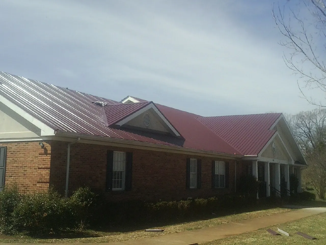 Red metal roof with gabled entries on a long brick building, from a Hail Damage Roof Repair job in Park Falls