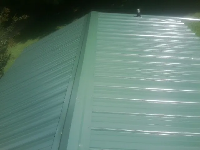 New green metal panels meeting at the ridge of a roof — Flat Roof Repair work by our crew in Park Falls