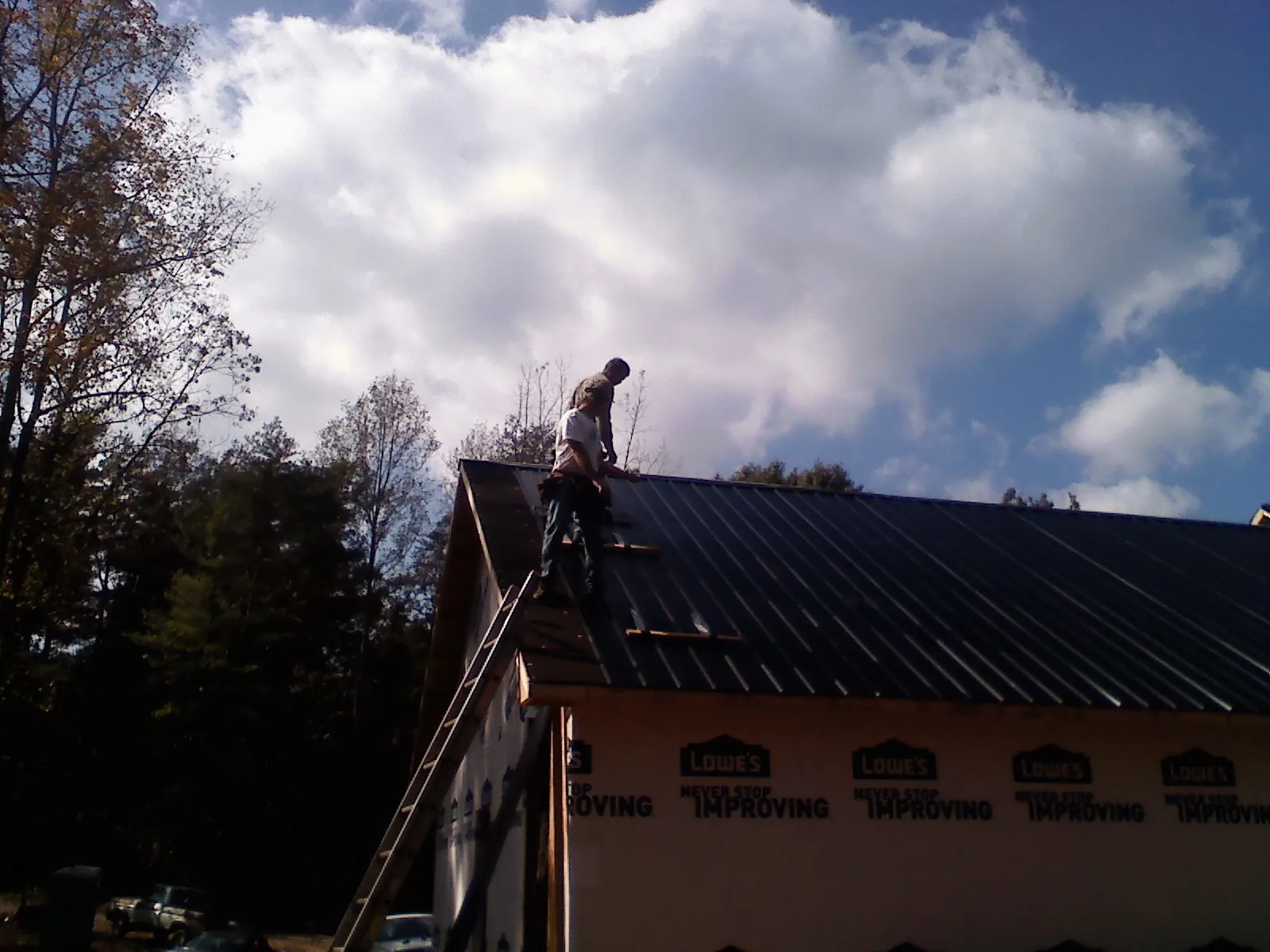 Roofer fastening dark metal panels high against a cloudy sky, from a Roof Inspection job in Park Falls