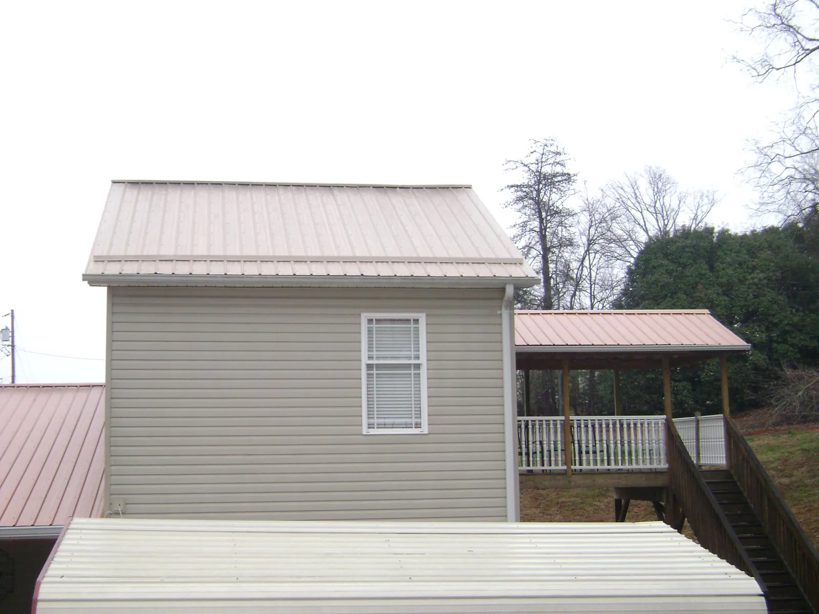 Tan metal roofs on a two story addition and attached porch, from a Roof Replacement job in Park Falls